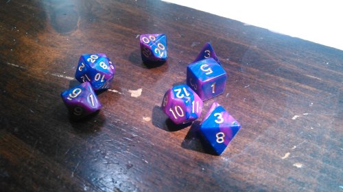 Some truly beautiful pinkish purplish dice with gold lettering lie on the table, waiting to be rolled against a Bugbear.